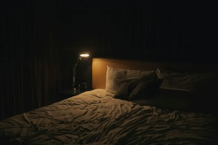 Lampada accesa accanto a un letto in una stanza in penombra